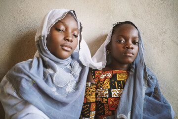 Two mourning black African sisters who symbolically seek protection under their mother's scarf;...
