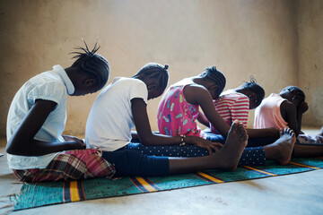 Side view of a group of frightened black African village girls sitting on the floor waiting for...