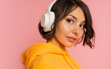 Studio photo of short haired brunette woman listenning music by earphones over pink background.