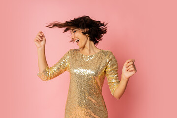Excited  woman in elergant golden sequin dress  dancing and  enjoing new year party. Pink background.