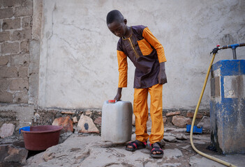 Neatly dressed young black boy fetching his family's daily water supply water at a public tap in...