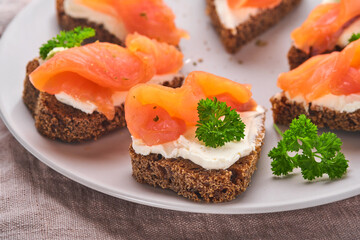 Mini sandwiches with salmon, curd cheese, parsley and rye bread in form of hearts. Valentine's day homemade creative food. Love breakfast design. Selective focus and copy space