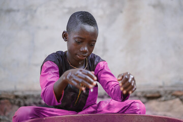 Cute black African boy sitting cross-legged in front of a plastic bathtub staring mesmerized at his...