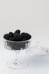 Fresh blackberries served in stylish patterned clear glass bowl on white background, concept of healthy eating vegan food. Closeup, side view, selective focus