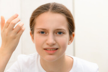 face of teenage girl, she looks at herself in the mirror and touches her face with her hand, she is upset and has frustrated emotions