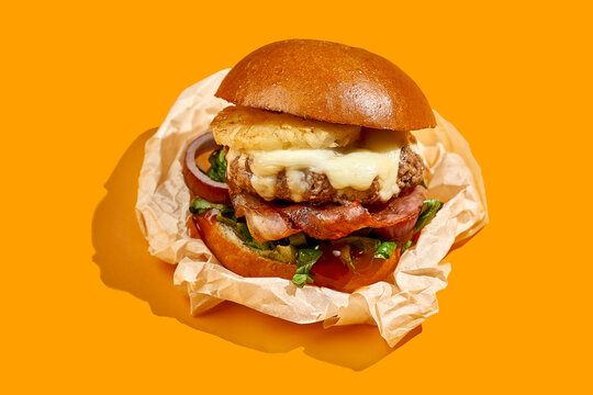 Appetizing burger with pineapple and cheese, bacon on a yellow background