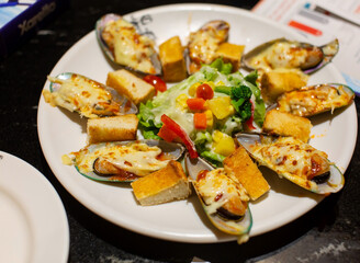 Eight slices of New Zealand mussels baked with cheese on a white round plate and green salad Close-up low side view focus on food
