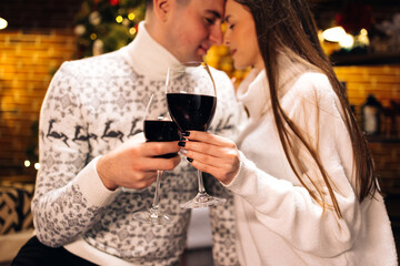 Love romance holiday celebration concept. Couple holding and drinking wine glasses sitting on sofa. Joy female and male toasting with red wine