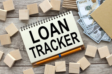 LOAN TRACKER. US dollars banknotes, open notepad with pen. Top view of the texture of expensive wood. wooden blocks near the notebook