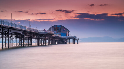 The long pier in the Mumbles, Swansea, south Wales. The wooden and steel structure sits in a calm sea, with a red sky behind it, at sunrise