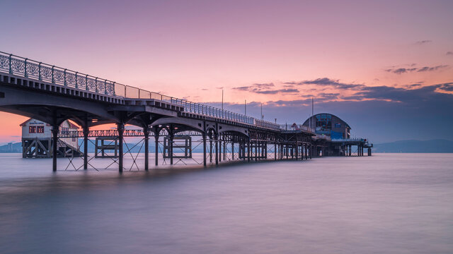 The long pier in the Mumbles, Swansea, south Wales. The wooden and steel structure sits in a calm sea, with a red sky behind it, at sunrise - Powered by Adobe