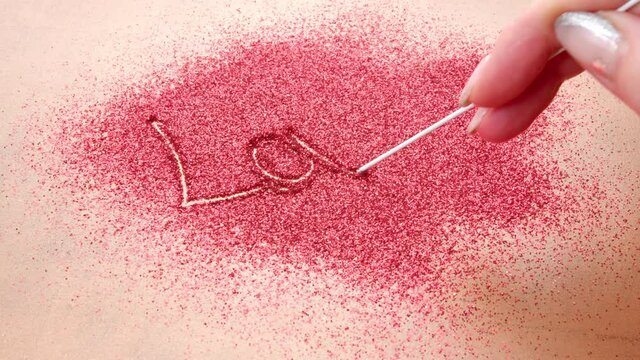 Woman Hand Writes Love . A woman hand writes love on bright red sand.