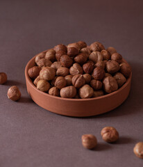Nuts, hazelnuts. Dish with peeled nuts on a brown background. Several nuts next to the dish. Selective focus. Close-up.