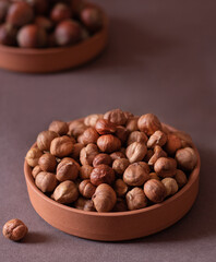 Nuts, hazelnuts. Shelled (peeled) hazelnuts on a brown platter, shell hazelnuts in a brown platter in the background. Beige background. Selective focus. Close-up.