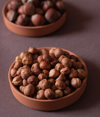 Nuts, hazelnuts. Shelled (peeled) hazelnuts on a brown platter, shell hazelnuts in a brown platter in the background. Beige background. Selective focus. Close-up.