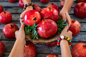 Hands of two females sharing and holding pomegranates on the platter.