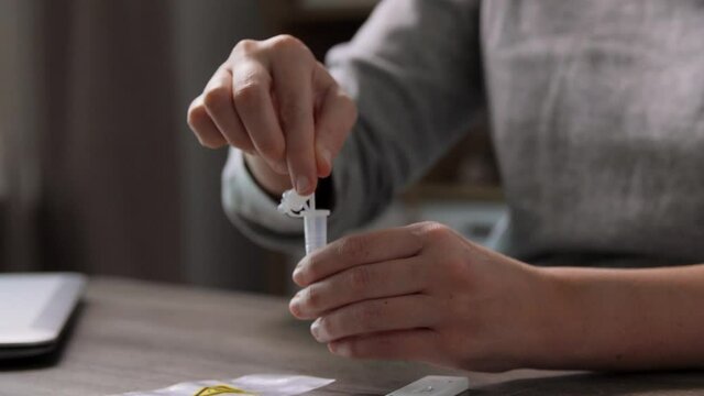 medicine, quarantine and pandemic concept - hands of woman making self testing coronavirus test and stirring swab in reagent at home