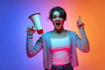 Excited young beautiful girl in warm cardigan shouting at megaphone isolated on gradient blue orange neon background - obrazy, fototapety, plakaty