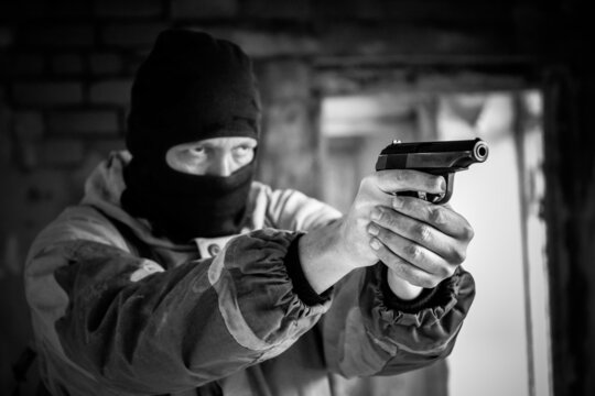A masked robber armed with a pistol is about to shoot. Armed attack, black and white photo, selective focus. Special police.