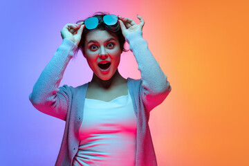 Studio shot of beautiful young girl waering sunglasses isolated on gradient blue-orange color...
