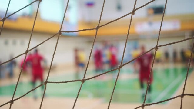 Player serves ball. Sport mesh on blurred background of competing people. Teamwork concept, selective focus.