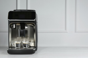 Modern espresso machine with cups of coffee on white wooden table near light wall. Space for text