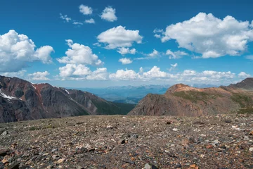 Foto op Canvas Beautiful mountain slope under blue cloudy sky, a view of a deep mountain valley with stunning snow peaks in the background. Awesome dramatic alpine view from pass to mountain valley. © sablinstanislav