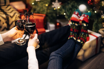 Adults people pouring wine into glasses for christmas and new year celebrations. Happy couple clink wine glasses toast and celebrate together New 2022 Year at home near glowing Christmas tree.