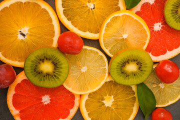 Healthy Food Background. Sliced fruits on a gray stone background. Citrus, orange, lemon, kiwi grapefruit, green leaves. Raw food diet. fresh ripe fruits as background