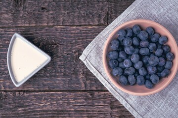 A bowl with blueberries on a gray cloth napkin and yogurt on a background of an old wooden surface. Close-up, flat lay