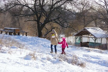 Mom and daughter are walking in the park by the lake on a warm sunny day. Walk on a winter day. Healthy lifestyle. Selective focus.