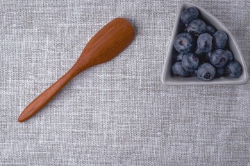 A ceramic bowl with blueberries and a wooden spoon on a gray tablecloth. Close-up, flat lay