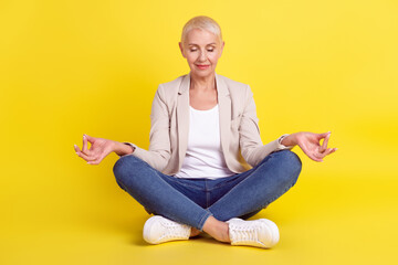 Full length photo of mature lady sit floor lotus pose meditate yoga asana isolated over yellow color background