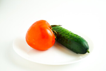 Cucumber and tomato are on a white plate. White background. The concept of healthy lifestyle.