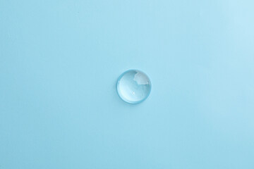 Drop of transparent ointment on light blue background, top view