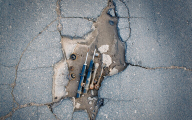 Broken damaged asphalt pavement, poor road maintenance. Damaged car suspension parts lay in road pot hole. Rusty suspension auto parts laid in asphalt hole.