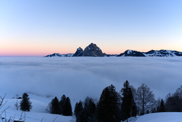Beautiful colored morning sky at mountain village Stoos with mountain panorama of Mythen mountains at wintertime. Photo taken December 21st, 2021, Stoos, Switzerland.