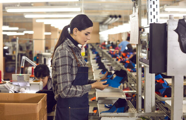 Side view of shoe factory worker standing in big sewing workshop and checking quality of unfinished...