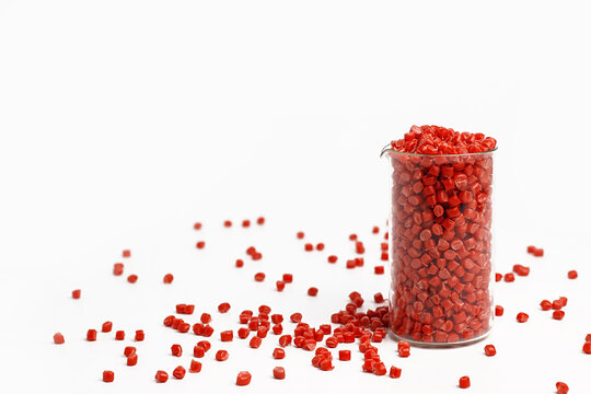 Red granules of polypropylene, polyamide in a measuring beaker and a test tube on a white background. Chemical products. Plastic, polymers and microplastics.