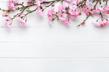 Fototapeta premium Cherry blossom on a white wood background. Floral frame border. Template with copy space. Romantic pattern with place for text. Mockup. Spring layout. Mother's day greeting card. Sakura branches.