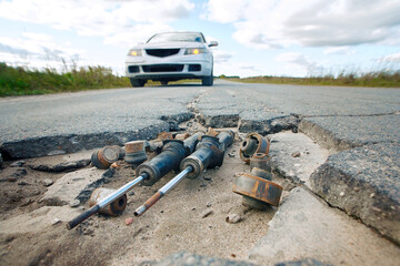 Damaged car suspension lies in road pot hole. Old and damaged suspension in asphalt hole, road...