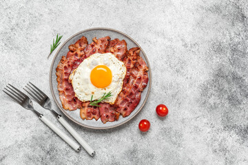 Fried egg with bacon on a plate, gray grunge background. Delicious appetizing breakfast. Top view, flat lay, copy space.