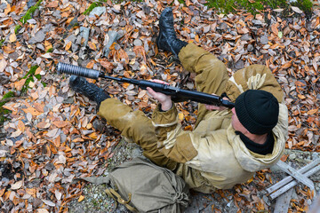 An armed soldier sits on the ground and aim from a machine gun, top view. A man in uniform shoots a...