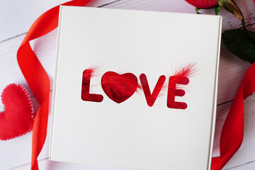 Gift box with red bow ribbon and word love on wooden table for Valentines day. copy space
