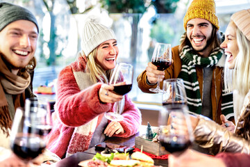 Young friends toasting red wine at restaurant patio - Happy people having fun together at winery bar wearing winter clothes - Dinning life style concept on bright filter with focus on left woman - 476579805
