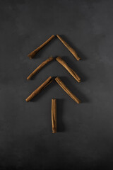 Simple Flat Lay with Christmas Tree made of Cinnamon Sticks on a Black Grunge Background. Modern Winter Holidays Decoration in the Soft Light of the Day ideal for Card, Banner, Greetings, Poster. 