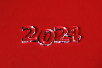 Fototapeta na wymiar Photo of numbers 2024 made of thick clear acrylic glass on a red background. Selective focusing.