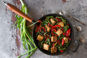 frying pan with stir fry with tofu, green beans and bell pepper on the table