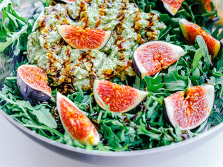 Fig salad with soft cheese and blueberries, avocado, arugula, balsamic sauce in steel bowl. Food closeup. Healthy vegetarian salad.