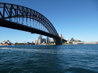 Sydney Harbour Bridge with Opera House and skyline in the background under a blue sky, Sydney, New...